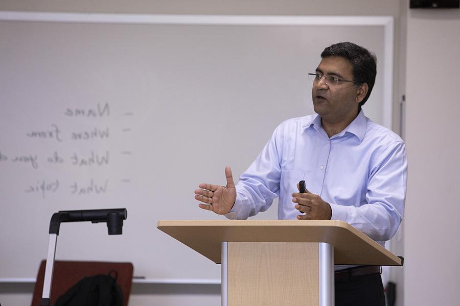 A faculty member teaches at the front of a classroom by a podium.