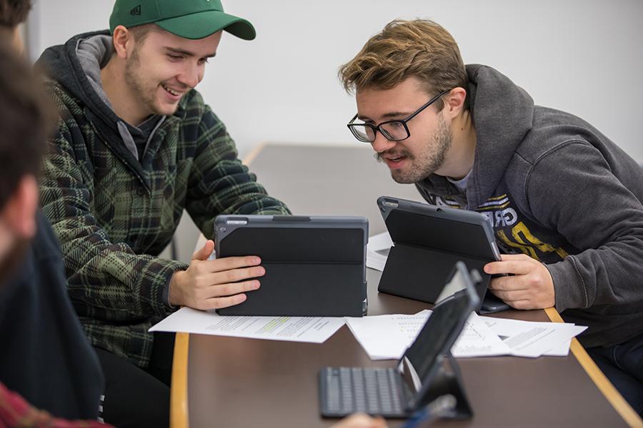 Two students work together on tablets in a classroom.